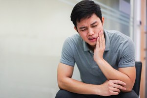 young man holds his mouth in pain