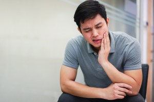 young man holds his mouth in pain